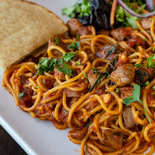 Spaghetti with meat sauce and fresh parsley, served with injera bread and a side salad.
