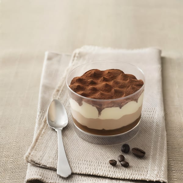 Layered tiramisu dessert in a glass cup with cocoa powder, a spoon, and coffee beans.