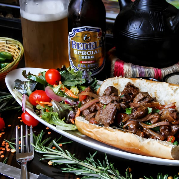 Desta Ethiopian Kitchen's Tibs sandwich with a side salad, Bedele beer, and traditional coffee pot.