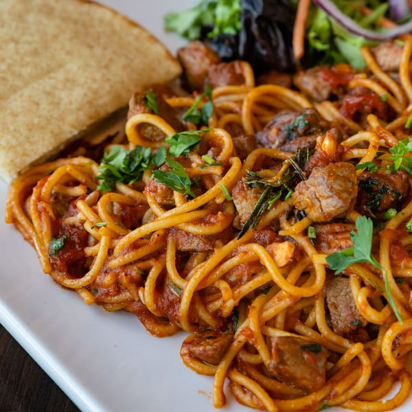 Spaghetti with meat sauce, garnished with fresh herbs, served with flatbread and a side salad.