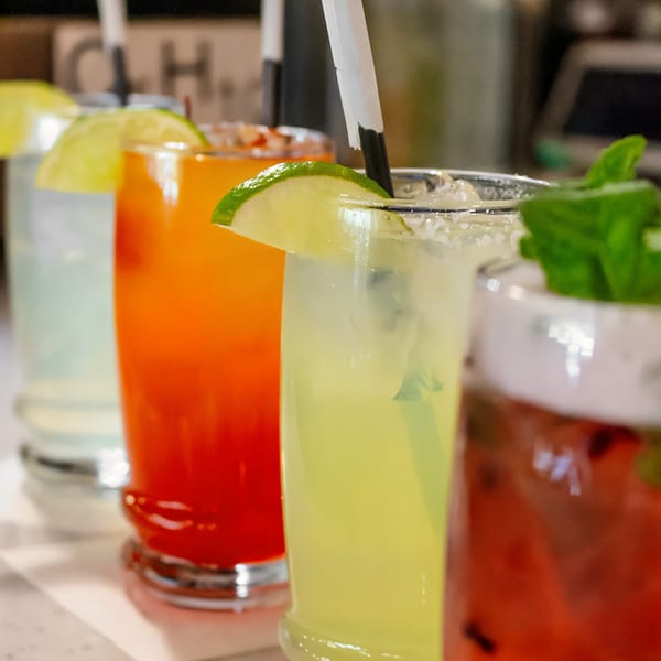 Four colorful cocktails, garnished with lime and mint, lined up on a bar.