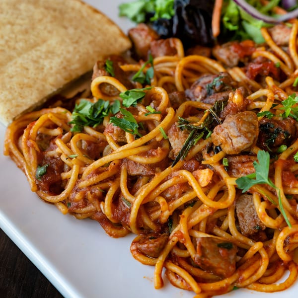 Spaghetti with meat sauce, garnished with parsley, served with injera bread and a side salad.