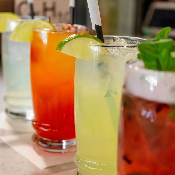 Four colorful drinks, including margaritas and cocktails, garnished with lime and mint.